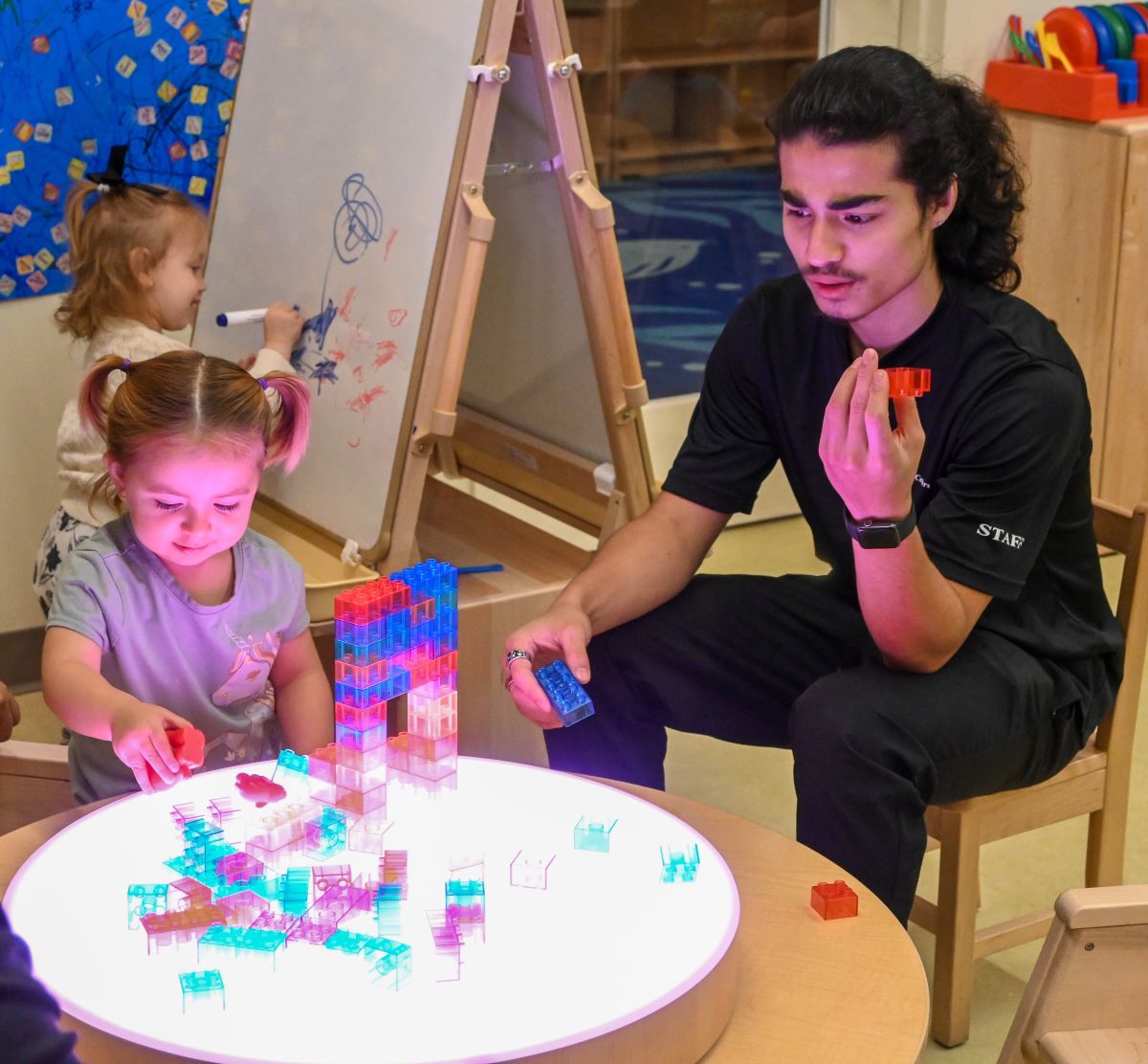 A teenage student helping a toddler play with blocks.