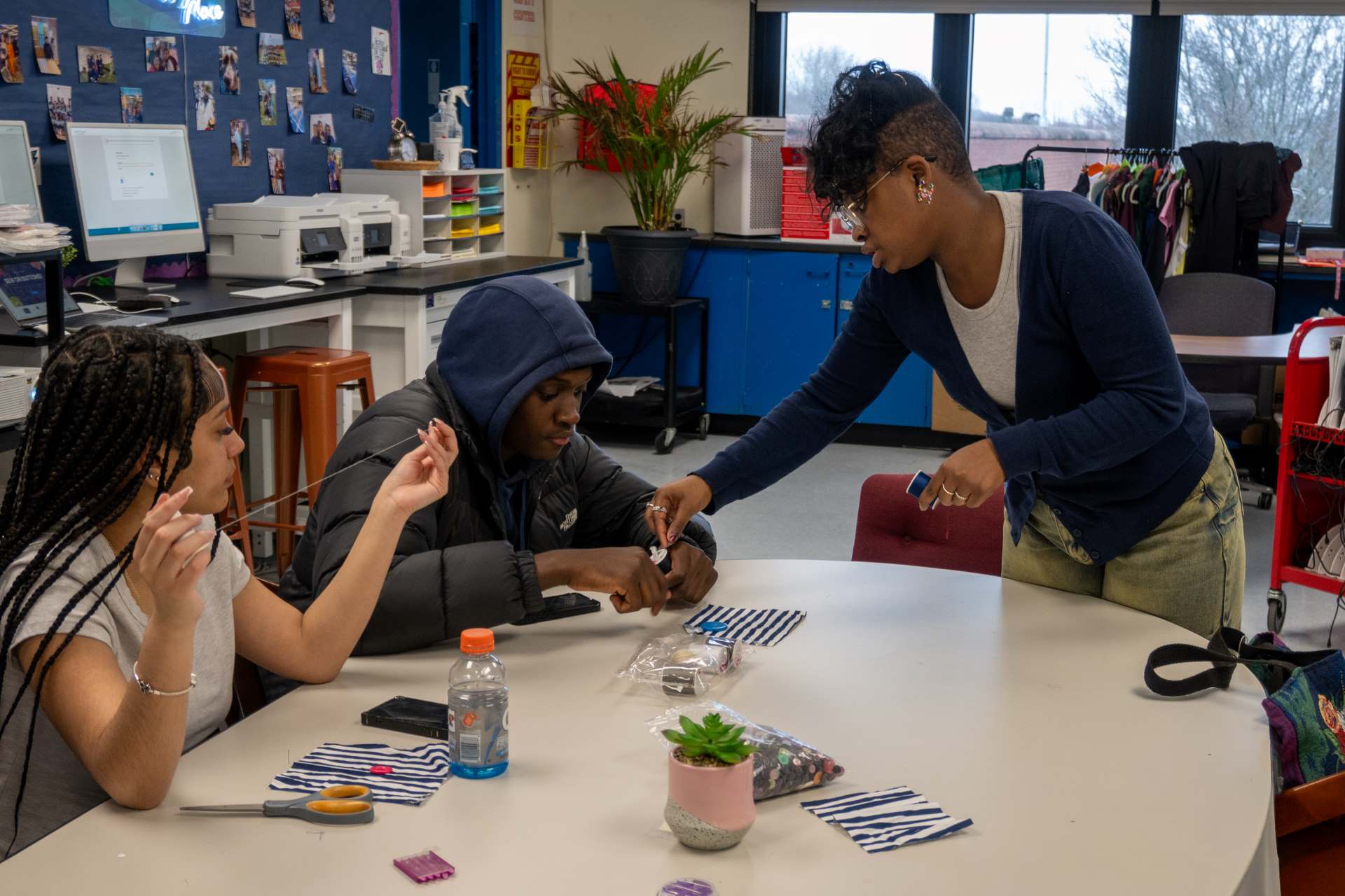 A teacher helps two students with a sewing project