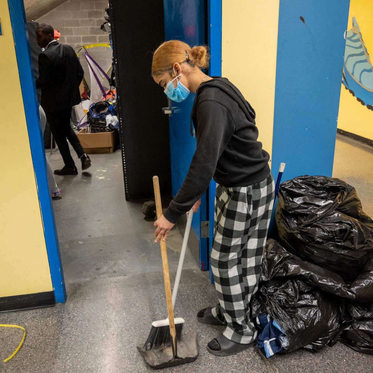 A student uses a dustbin and broom to clean an athletic storage room